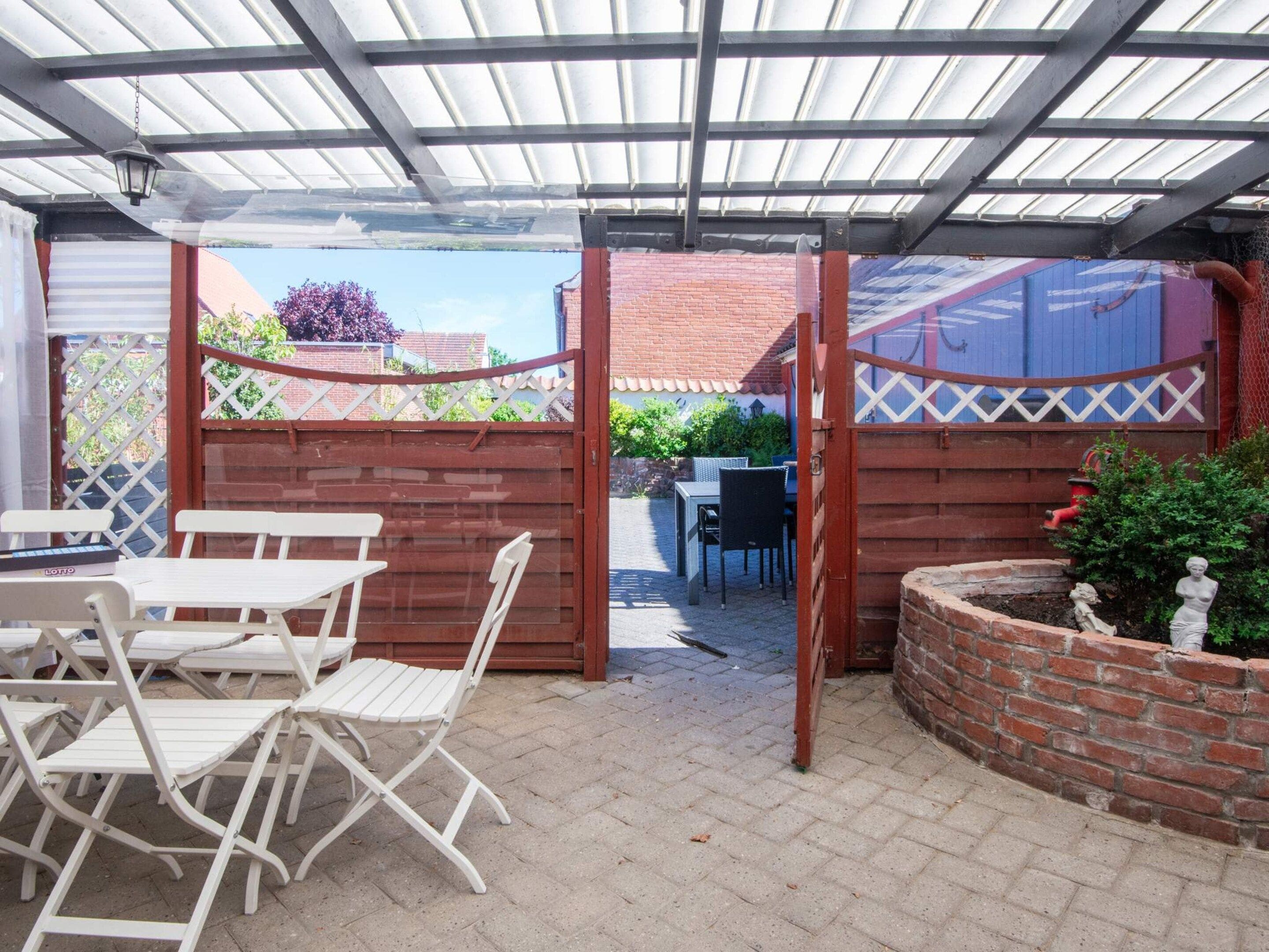 A covered patio area with a table and chairs, a brick wall, and a view of the street.