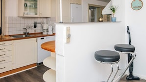 A kitchen with a sink, coffee maker, and cabinets. There are two stools and a vacuum cleaner. - 12 Person Holiday Home in Ringkobing (Ringkobing)