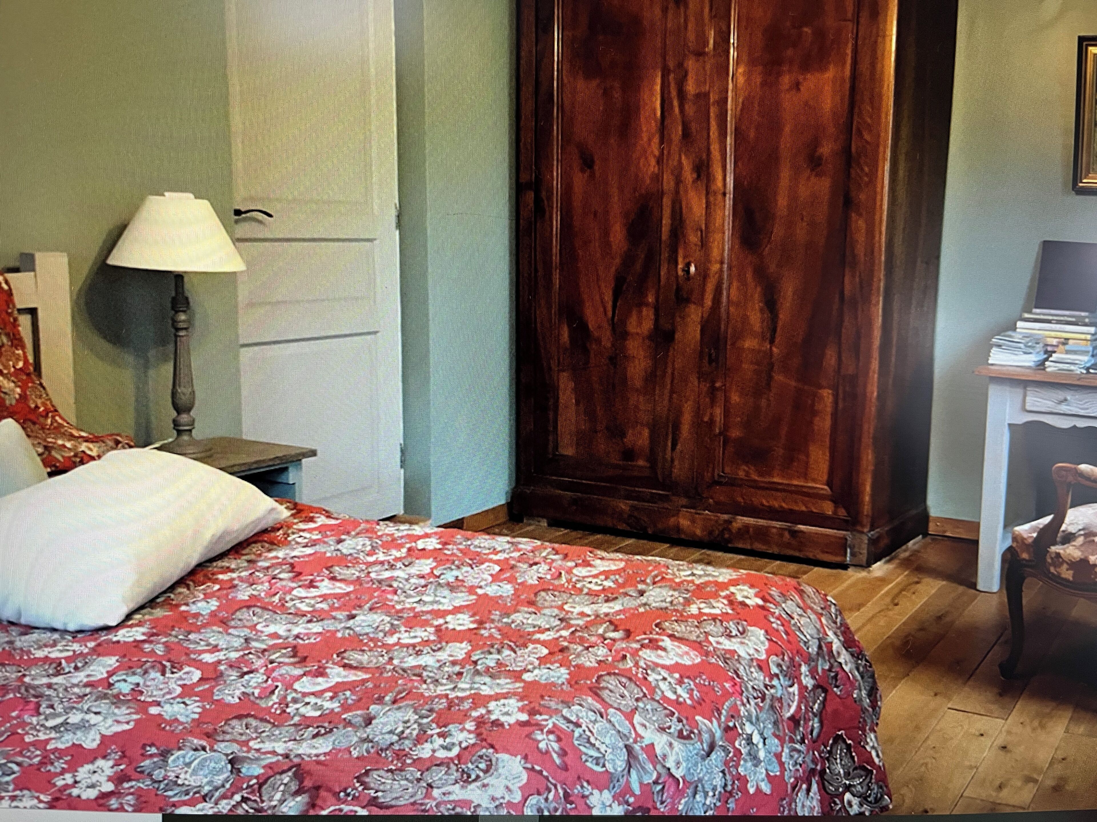 Een slaapkamer met een bed, een houten garderobe, een nachtkastje, een lamp en een stoel.
