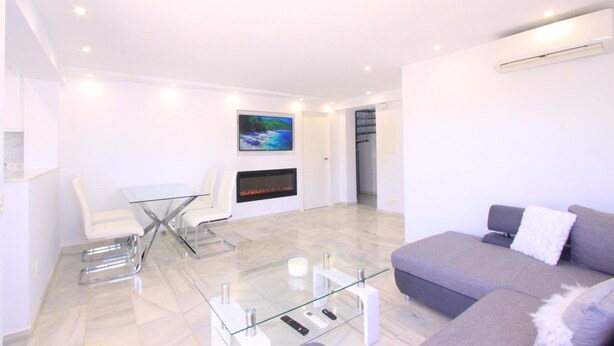 A modern living room with a glass coffee table, white chairs, a grey sofa, and a fireplace. - Beachfront Penthouse With Pool Access (Marbella)