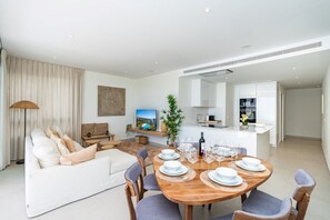 A modern living room with a dining area, a sofa, a TV, and a kitchen in the background. - 6-guest Apartment Near Golf Course (Estepona)