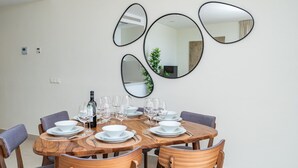 Comedor con mesa de madera dispuesta para seis personas, rodeada de seis sillas. Hay cuatro espejos en la pared y una planta en maceta.