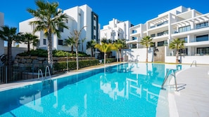 A modern hotel with a swimming pool, palm trees, and white buildings. - 6-guest Apartment Near Golf Course (Estepona)