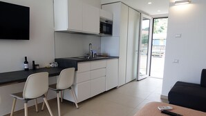 Una cocina compacta de diseño moderno, con horno empotrado, lavamanos y microondas. Hay dos sillas y una mesita con un control remoto encima.