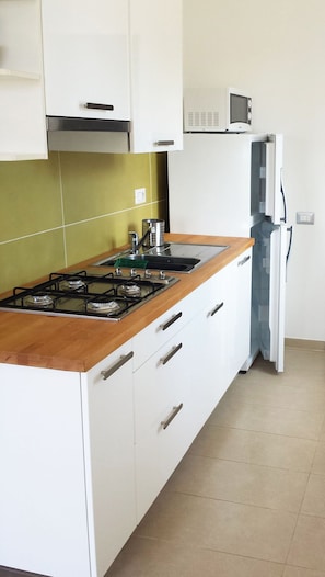 A kitchen with a gas stove, white cabinets, a microwave, and a refrigerator. - Hotel Residence Il Faro Acciaroli (Acciaroli)