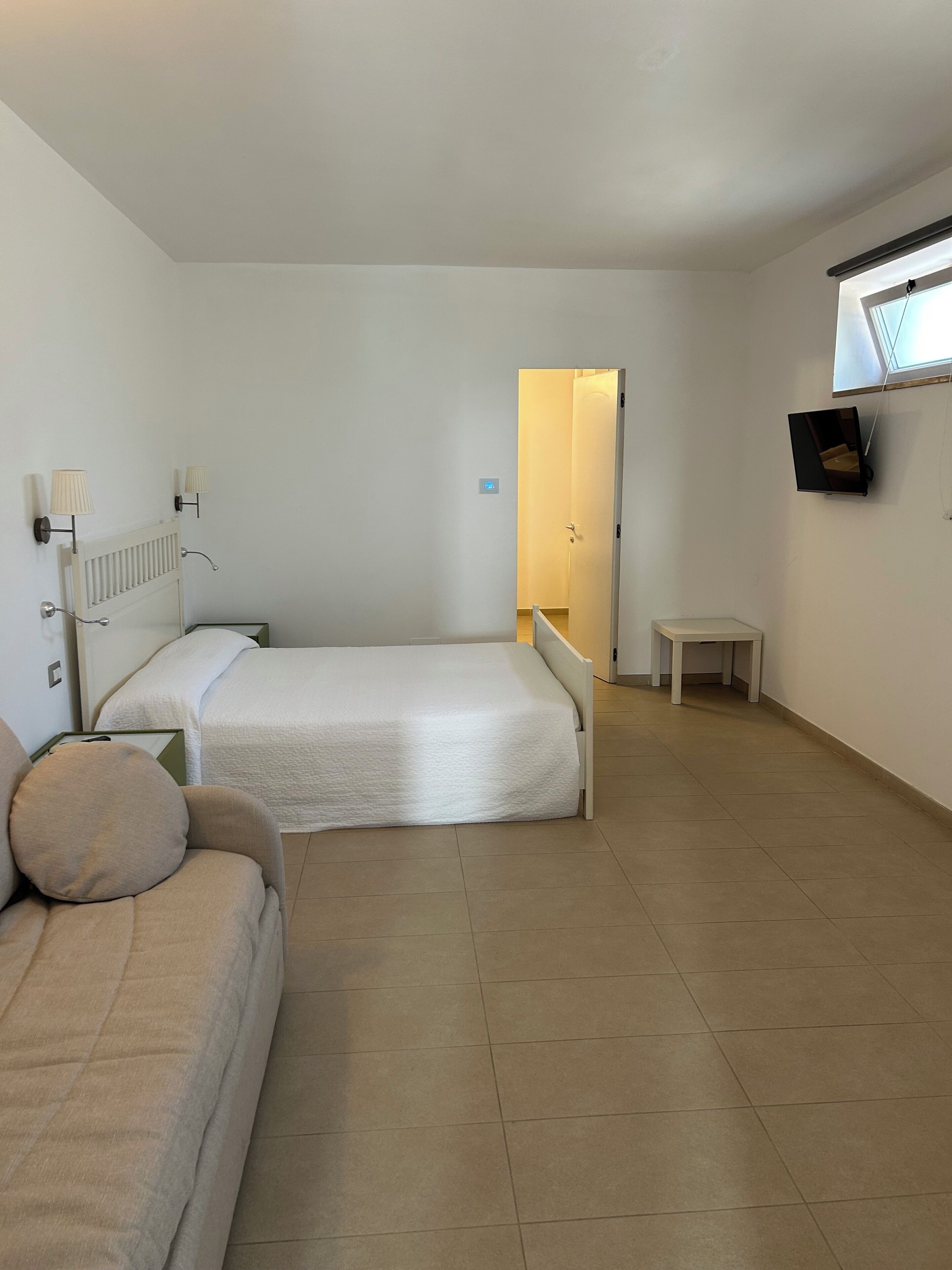 Camera d'albergo con un letto, un tavolino, una TV a parete e un termosifone.
