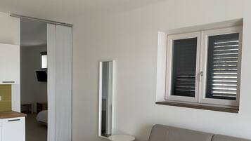 Una sala de estar moderna con un sofá, una mesa de comedor con sillas, una zona de cocina y una ventana con persianas.