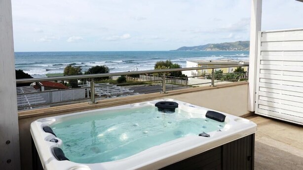 Un jacuzzi en un balcón con vistas al océano y colinas.