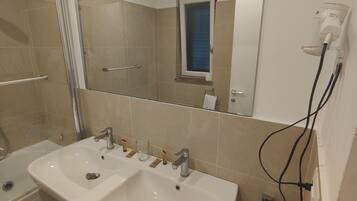 Een moderne badkamer met twee wasbakken, een grote spiegel en een haardroger op de muur.
