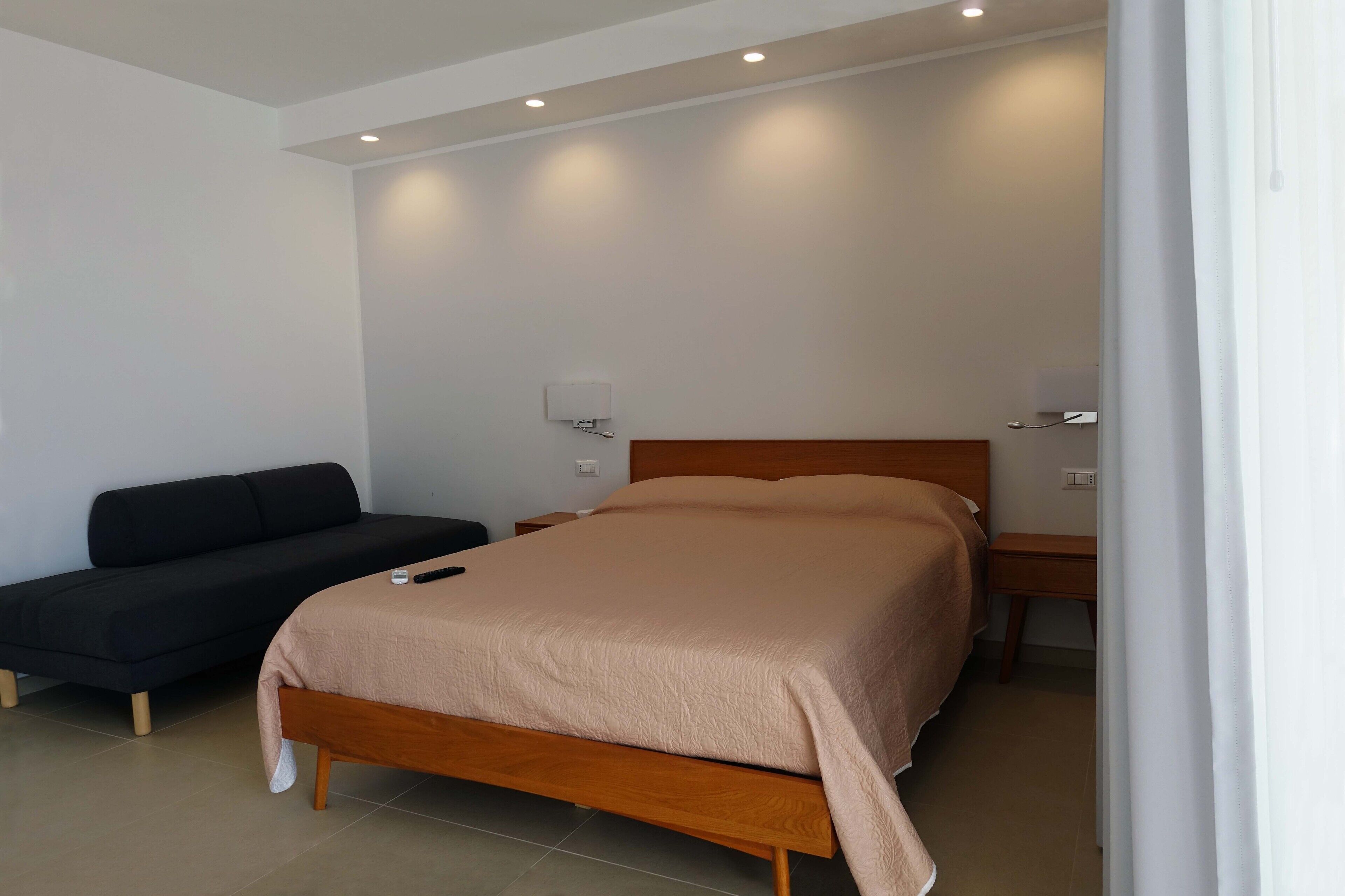 A modern bedroom with a bed, a sofa, and two bedside tables.