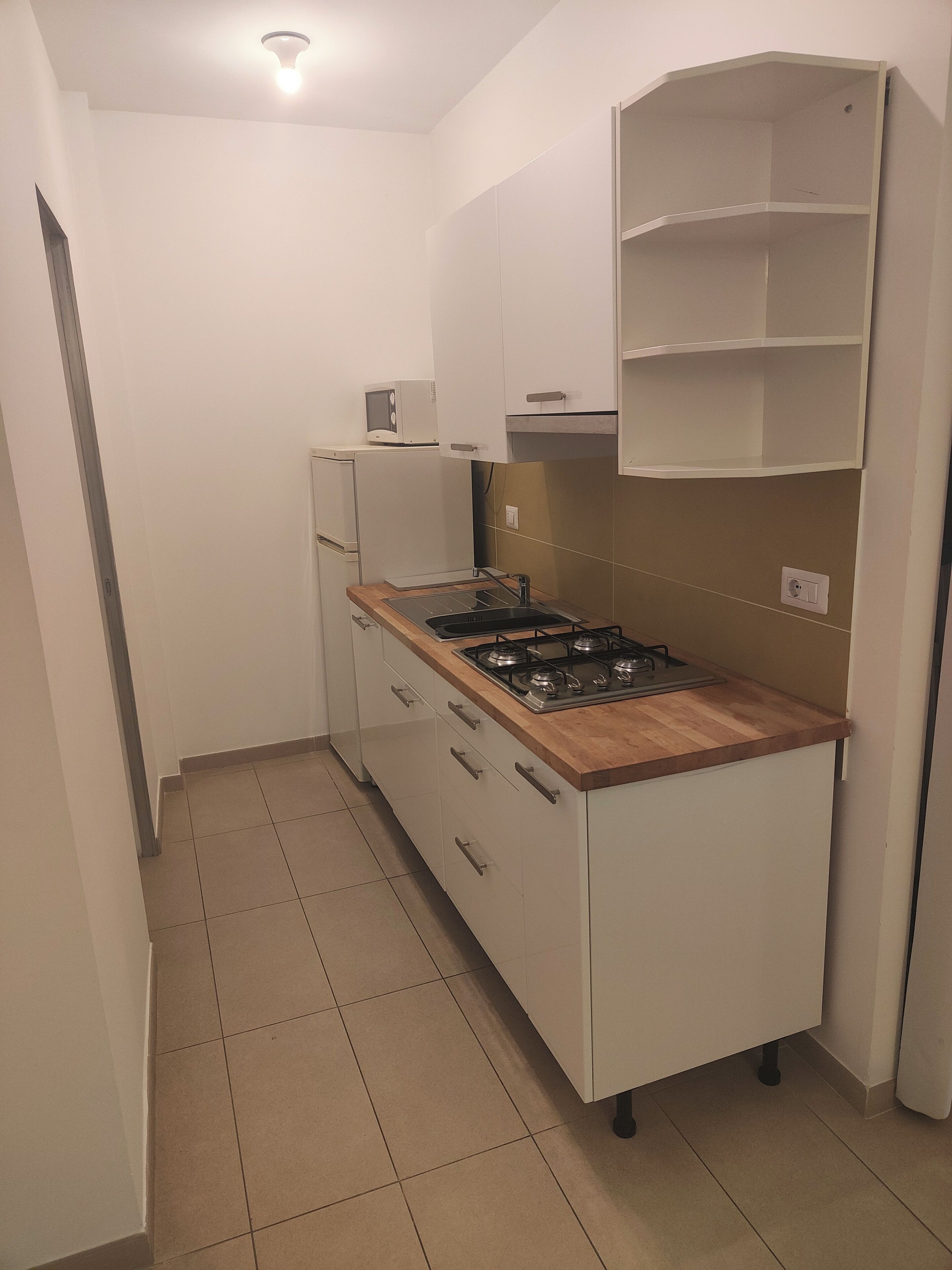 Eine kleine Küche mit einem Gasherd, einer Mikrowelle und einem Kühlschrank.