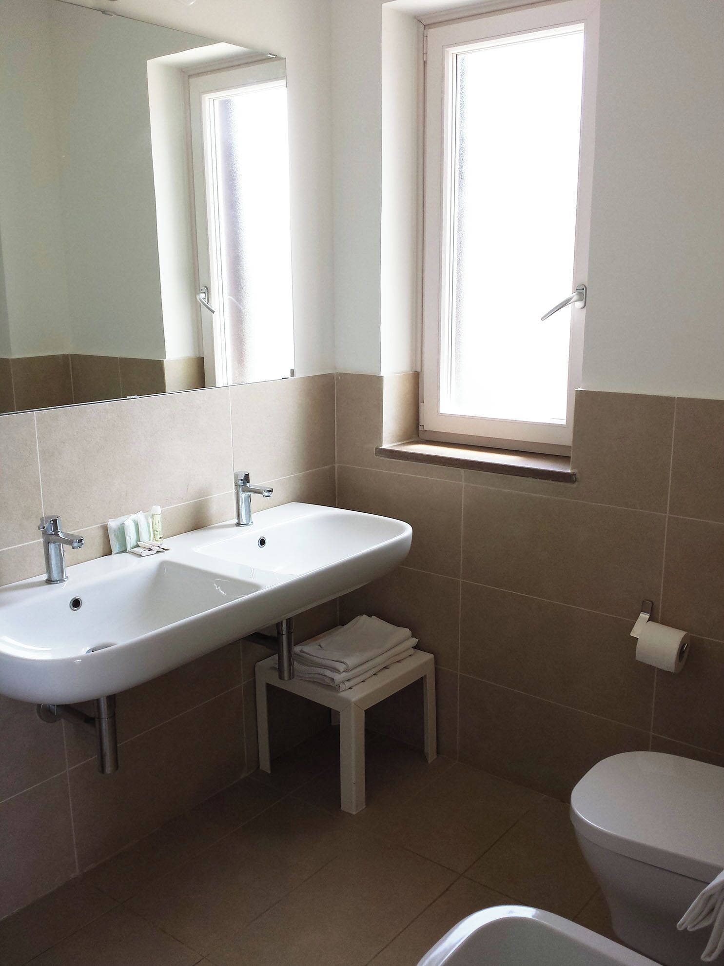 Ein Badezimmer mit einem Doppelwaschbecken, Toilette, Fenster und Spiegel.