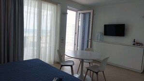 Una habitación de hotel con cama, televisor, mesa de comedor y sillas, y un balcón con cortinas.
