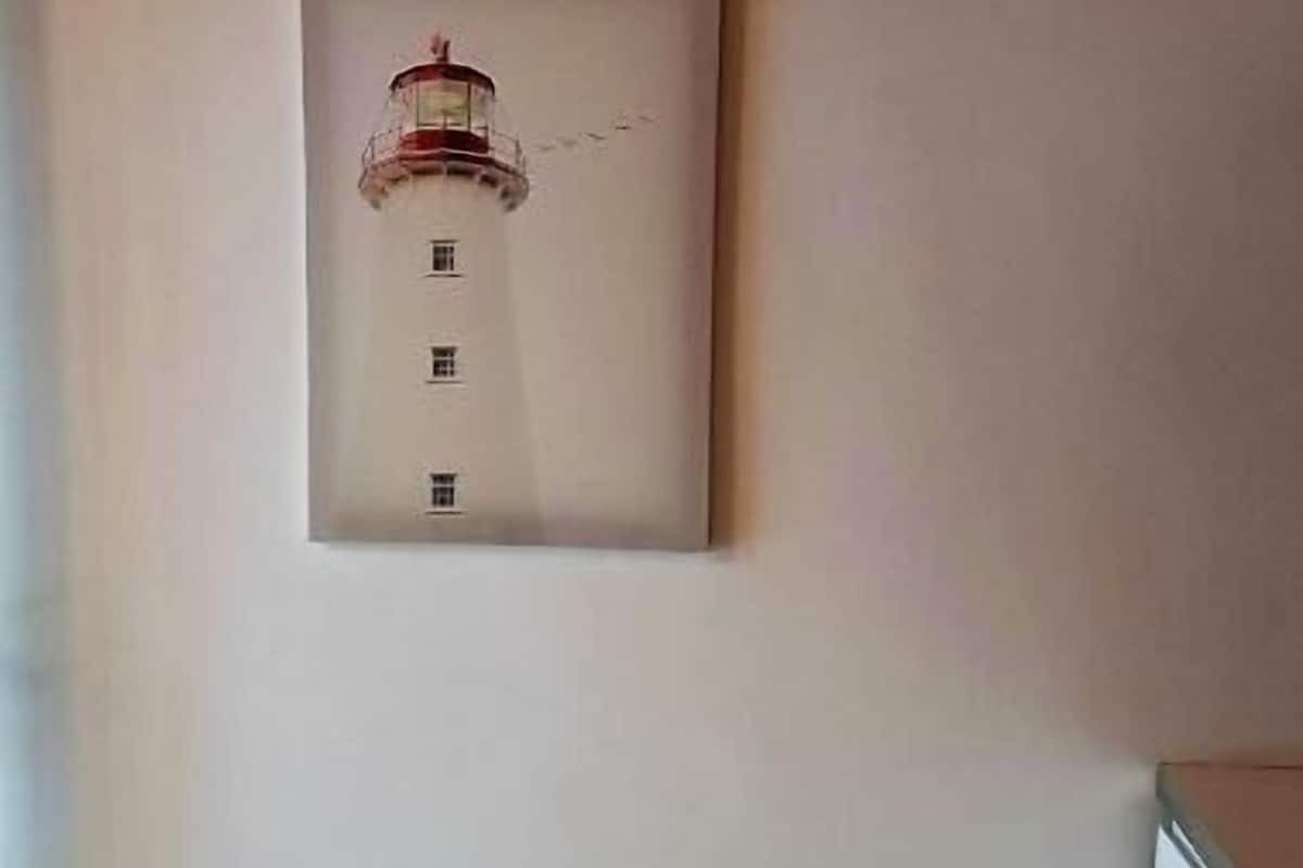 A framed picture of a lighthouse on a plain wall in a room with tiled flooring and a white cabinet.
