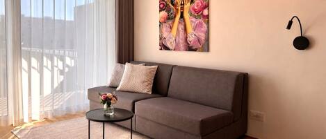 Una sala de estar con un sofá gris, una mesa redonda de centro con un florero y un cuadro en la pared.
