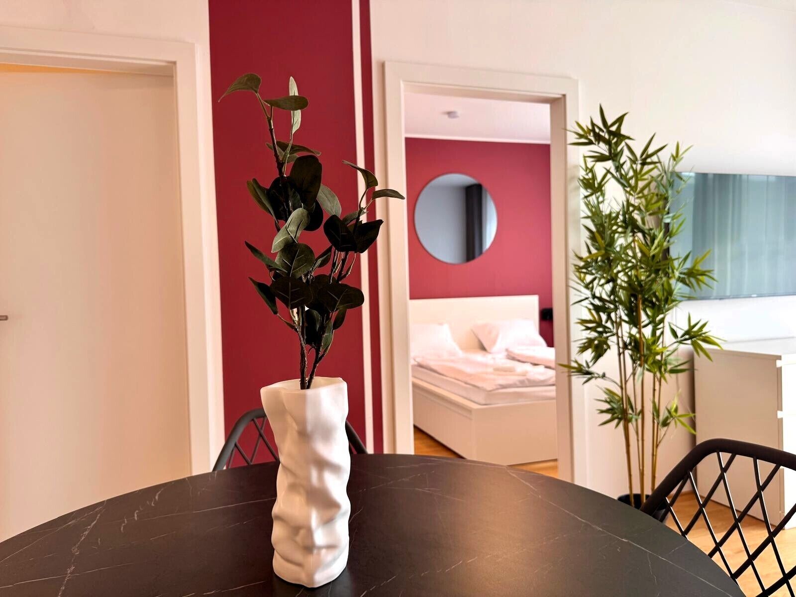 Een kamer met een bed, een ronde spiegel en een eettafel met stoelen.
