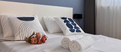 A hotel room with a bed, two pillows with geometric designs, a bouquet of roses, and a neatly folded towel.