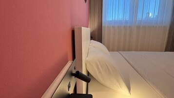 Una habitación de hotel con cama, mesita de noche con toma de corriente y ventana con cortinas.