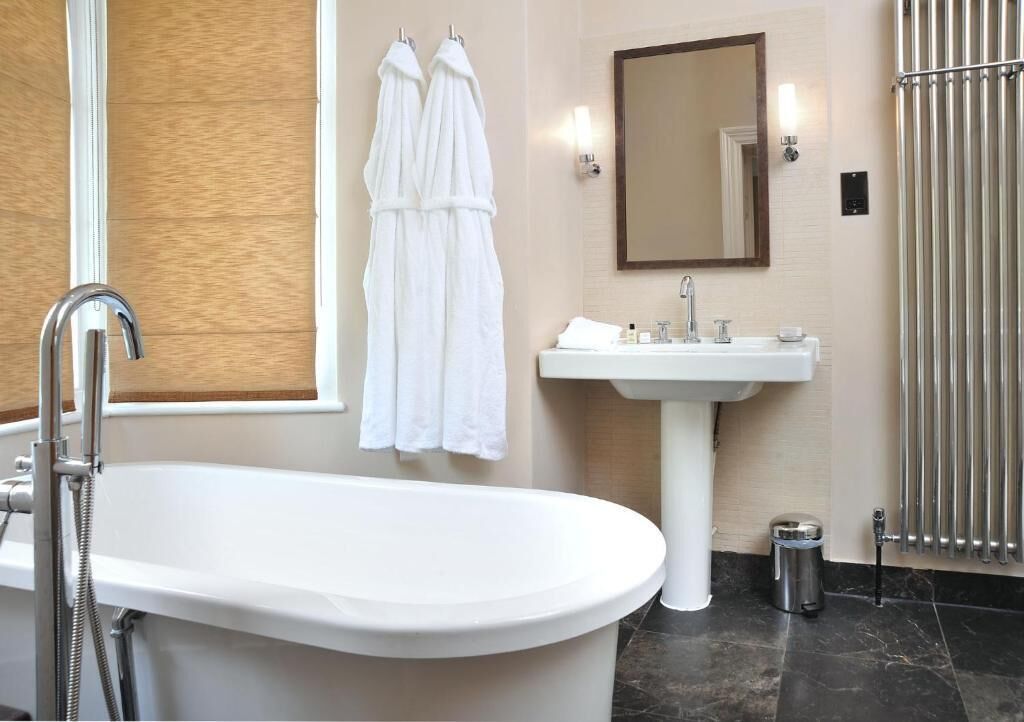 Ein Badezimmer mit freistehender Badewanne, Waschtisch, Spiegel und einem Handtuchhalter mit zwei Handtüchern.