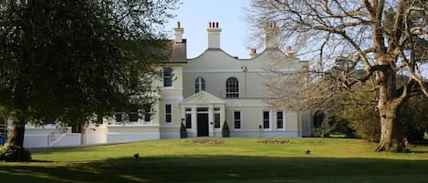 A large, stately building with a symmetrical facade, a central entrance with columns, and a well-maintained lawn in front.