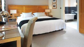 Habitación de hotel con una cama grande, dos mesitas de noche con lámparas, un escritorio con silla y un baño visible a través de una puerta abierta.