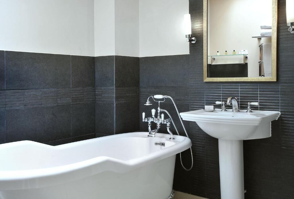 A modern bathroom with a freestanding bathtub, a pedestal sink, and a wall-mounted mirror.