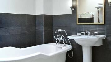 A modern bathroom with a freestanding bathtub, a pedestal sink, and a wall-mounted mirror.