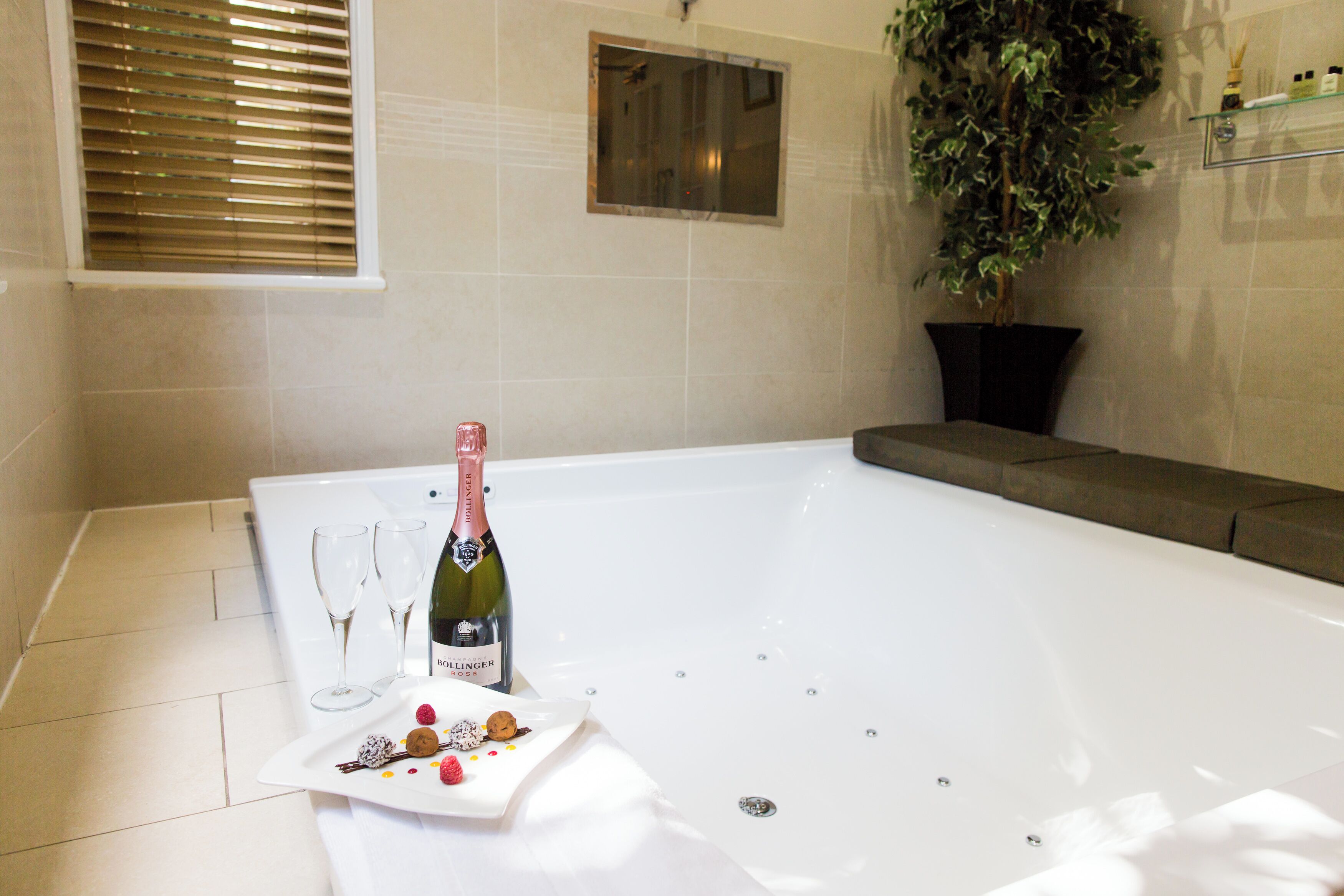 A bathroom with a bathtub, a bottle of champagne, and a plate with snacks.