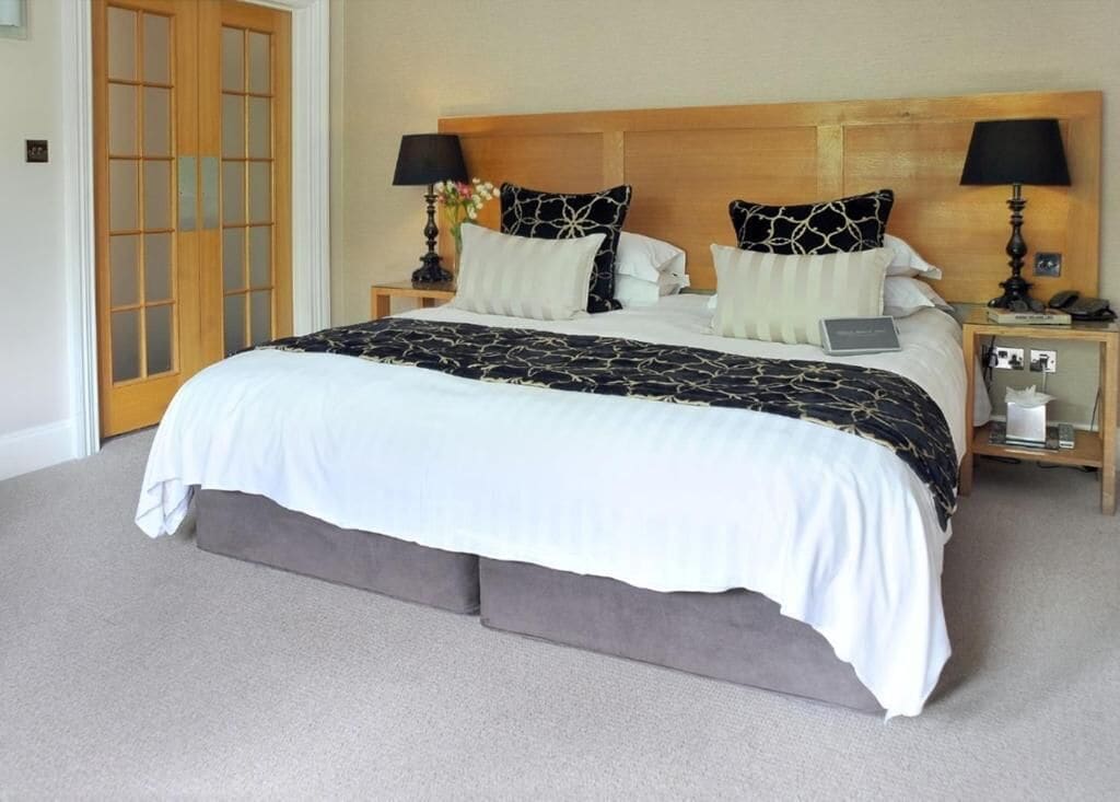Una cama grande con una colcha de diseño blanco y negro, dos mesitas de noche con lámparas y un cabecero de madera.