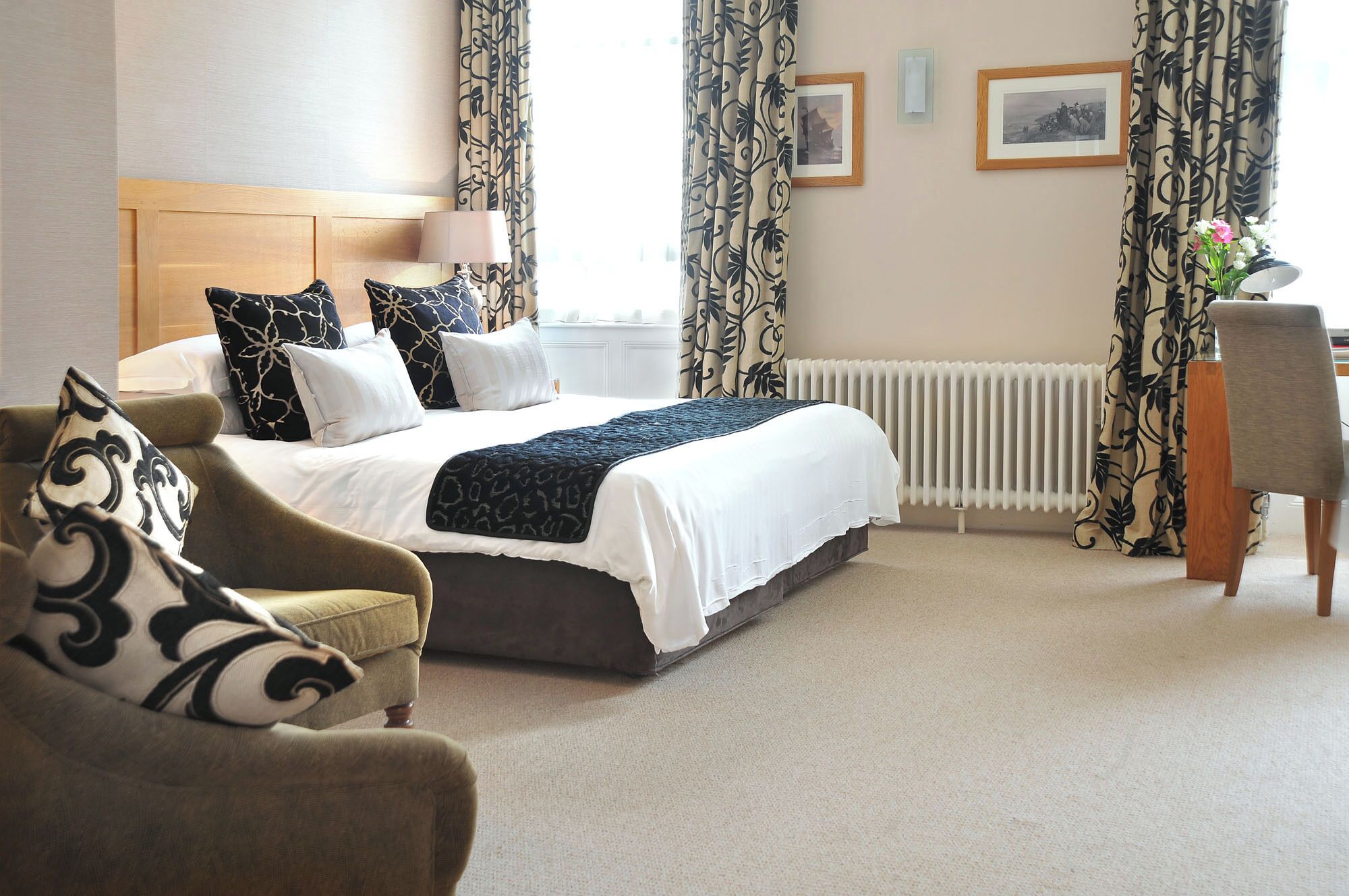 A hotel room with a bed, a chair, a desk, a radiator, and curtains.
