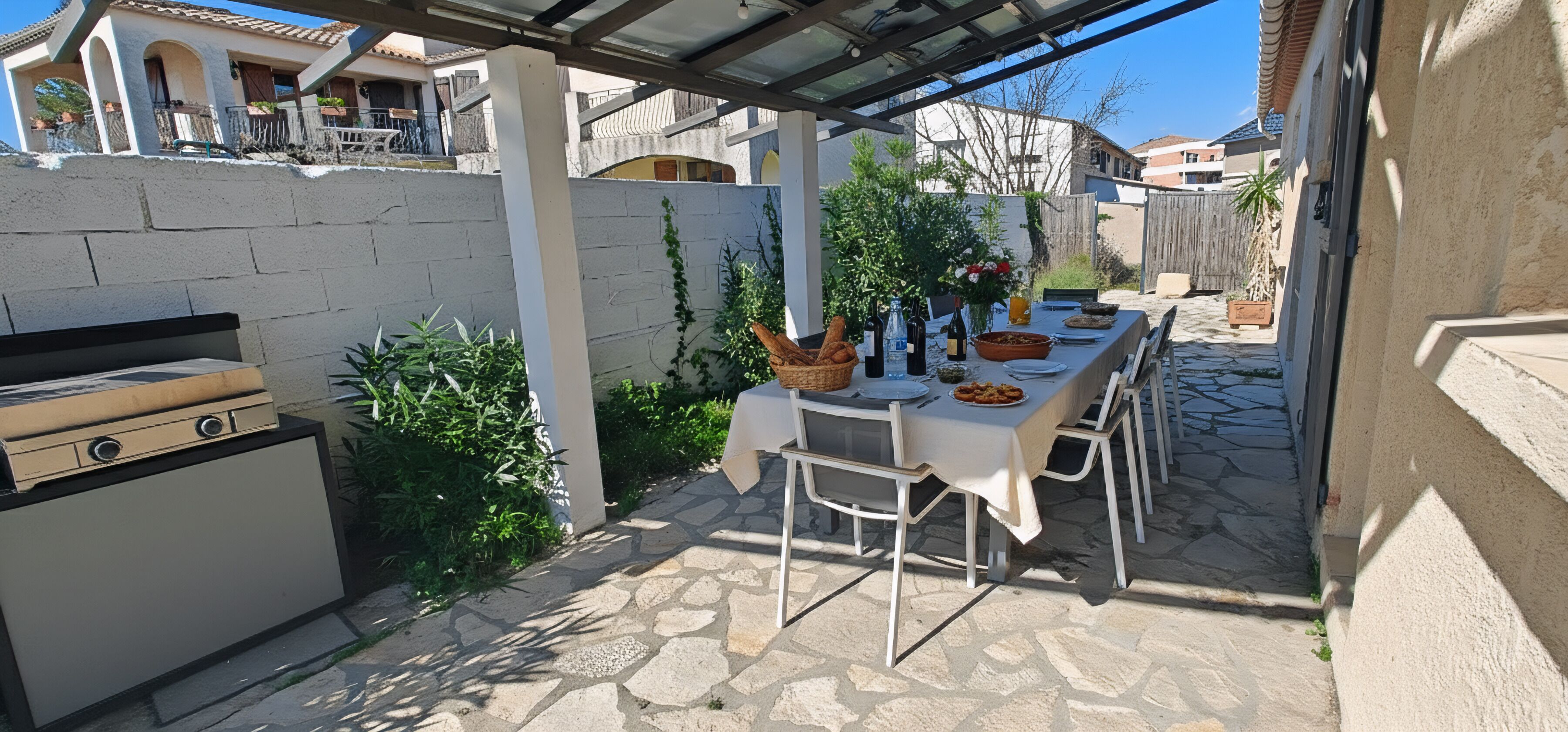 An outdoor patio with a grill, a table set for dining, and a stone pathway.