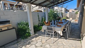 Eine Außenpatio mit Grill, einem Esstisch und einem gepflasterten Weg.