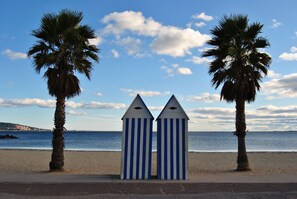 Duas cabanas de praia listradas, com uma praia e palmeiras ao fundo.