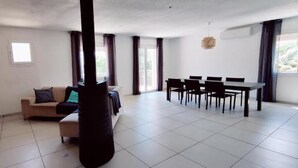Un grand espace de vie comprenant un canapé, une table à manger avec des chaises, un téléviseur et une grande fenêtre.