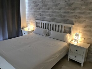 A neatly made bed with white linens, two bedside tables with lamps, and a wooden wall behind the bed. - 5-guest Apartment Near Alcazaba Lagoon (Casares)
