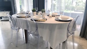 Una mesa redonda de comedor con mantel blanco, sillas transparentes y cristalería.
