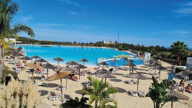 Un resort frente a la playa con una piscina grande, tumbonas, sombrillas y vistas despejadas al océano.