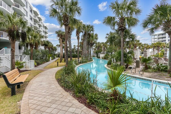 A pool area with palm trees, a pathway, and a bench. - 2400 Sq Ft | Sleeps 12 | 700ft Lazy River Retreat (Fort Walton Beach)