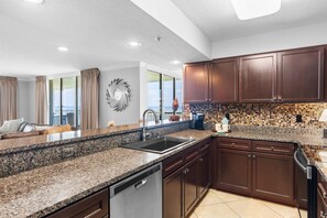 A modern kitchen with granite countertops, dark wooden cabinets, and a large window offering a view.