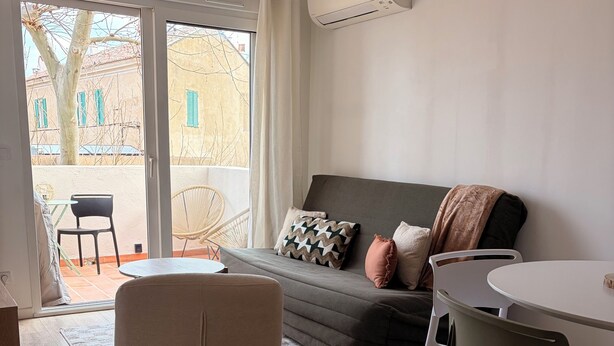 Un soggiorno moderno con un divano, poltrone, un tavolo da pranzo e vista su una zona esterna tramite una porta scorrevole in vetro.