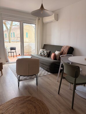 A modern living room with a sofa, chairs, a dining table, and a view through a sliding glass door to an outdoor area. - Apartment in the heart of Algajola village with sea view (Algajola)