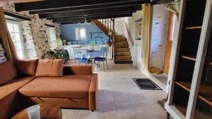 Una sala de estar acogedora con un sofá, un comedor con una mesa y sillas, una cocina al fondo y una escalera que sube.