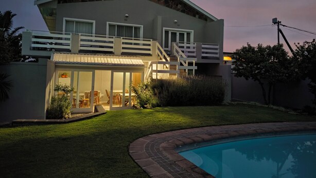 Ein zweistöckiges Haus mit Balkon, Schwimmbad und einem gut beleuchteten Patio.