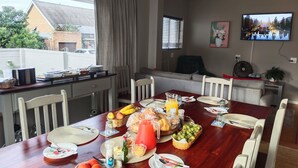 Ein Essbereich mit einem Holztisch, gedeckt für eine Mahlzeit, einem an der Wand befestigten Fernseher und Blick ins Freie.