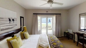 Ein Hotelzimmer mit einem Bett, einem Schreibtisch, einem Stuhl, einem Deckenventilator und einem großen Fenster mit Vorhängen.
