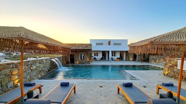 A poolside area with lounge chairs and a stone wall. - Mykonos Dot - Art Homes (Ano Mera)