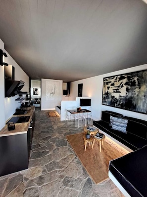 Ein modernes Interieur mit Steinboden, einer schwarzen Couch, einem Essbereich und einer Küche mit schwarzem Arbeitsplatz.
