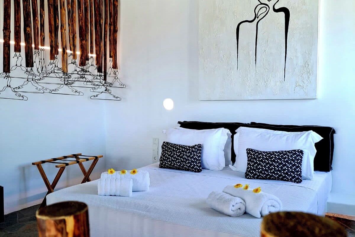 Een slaapkamer met een bed, kussens, handdoeken, een houten kunstwerk en een abstract schilderij aan de muur.