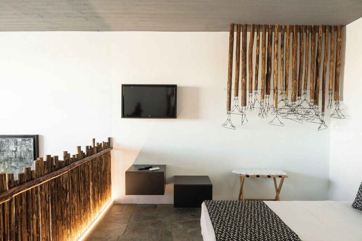 A modern bedroom with a wooden accent wall, a mounted TV, a small ironing board, and a bed with patterned bedding.
