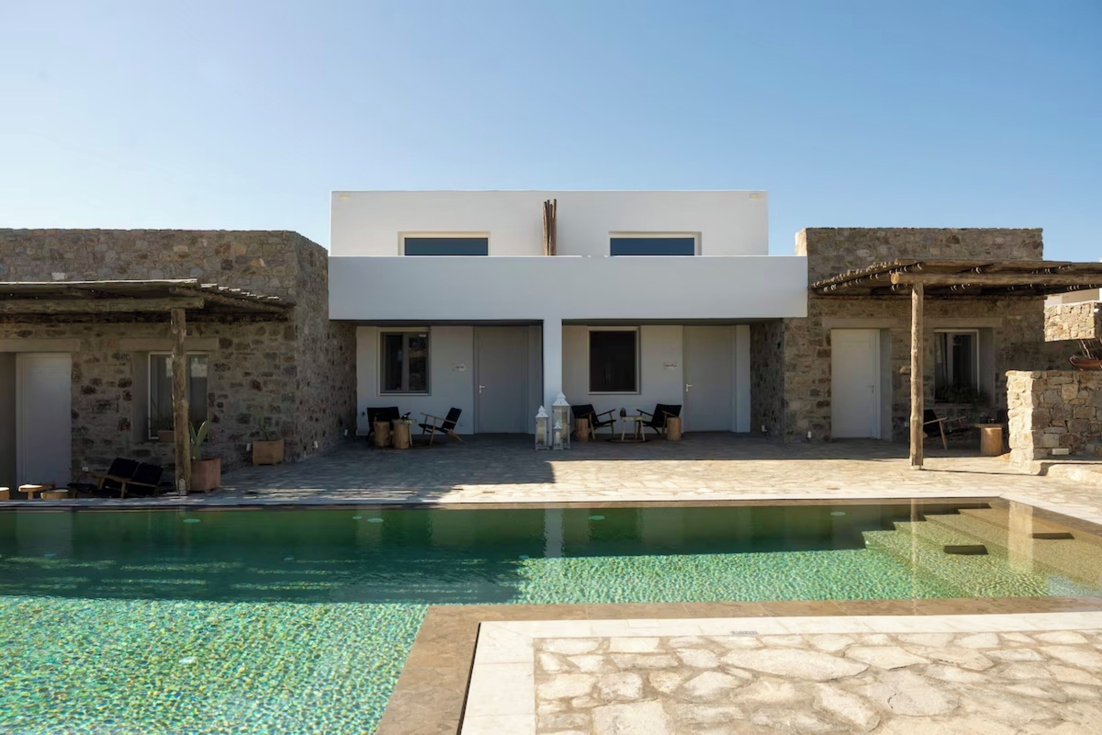 A modern building with a pool, stone walls, and outdoor seating.